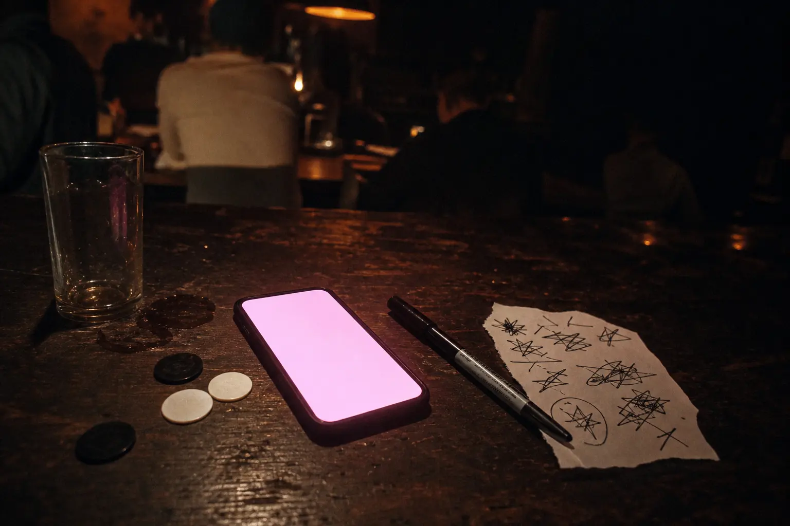 A phone glowing pink on a bar top next to a marker and a scribbled setlist